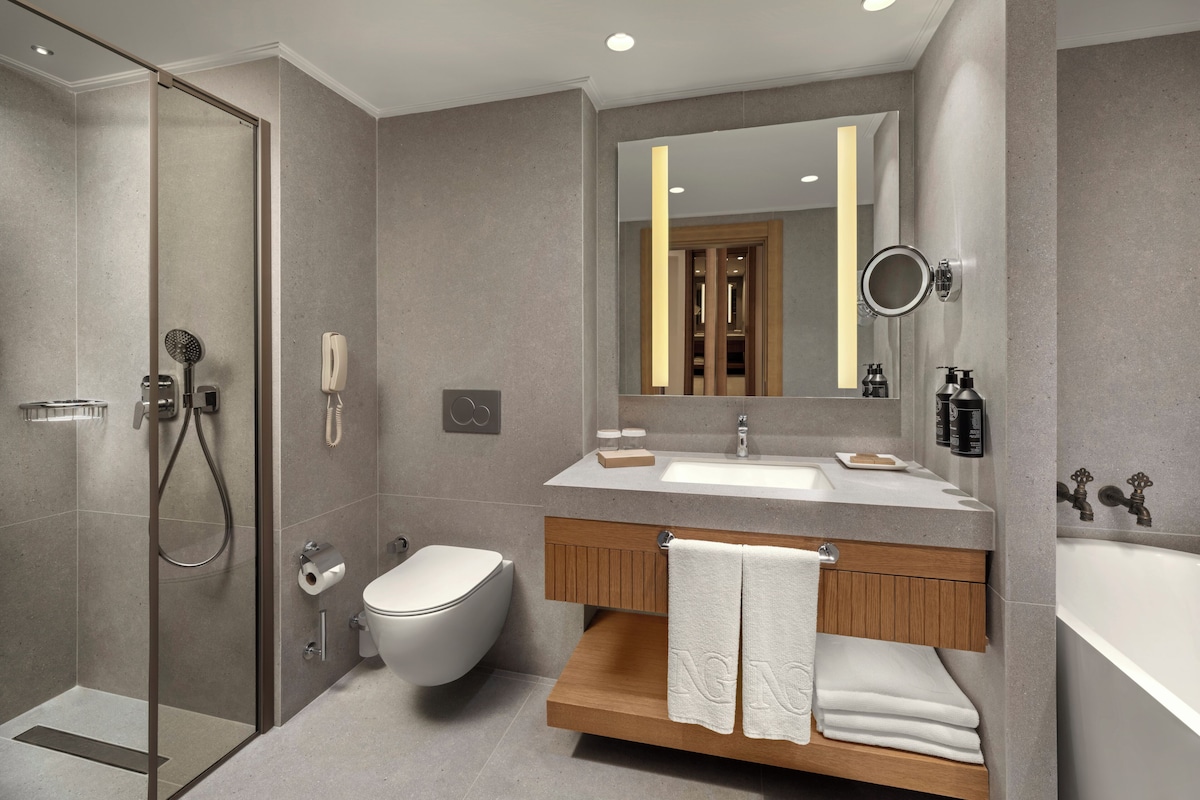 Un baño moderno con ducha de vidrio, inodoro, lavamanos con tocador y un espejo grande.