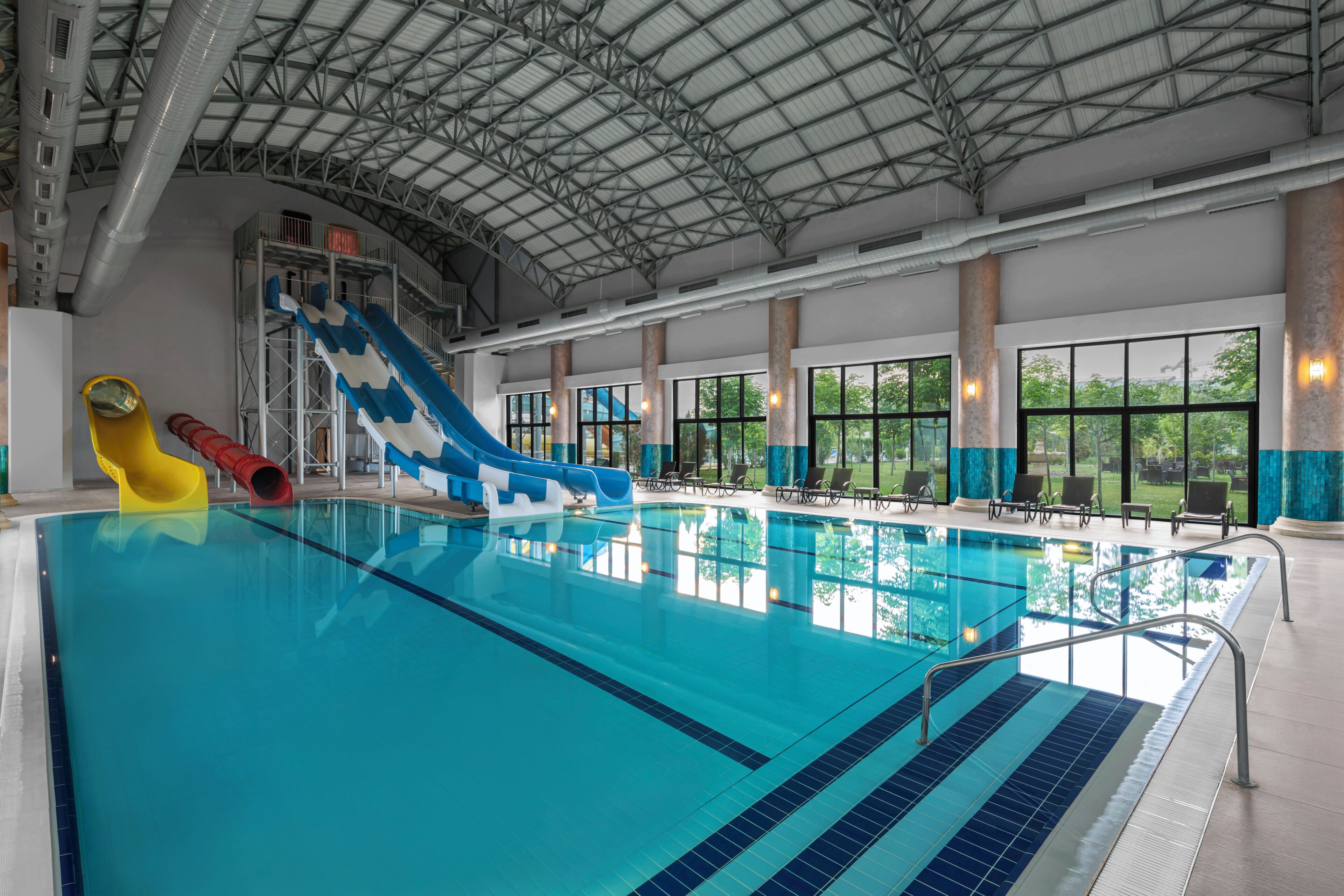 Piscina interior con toboganes y vistas al exterior a través de amplios ventanales.