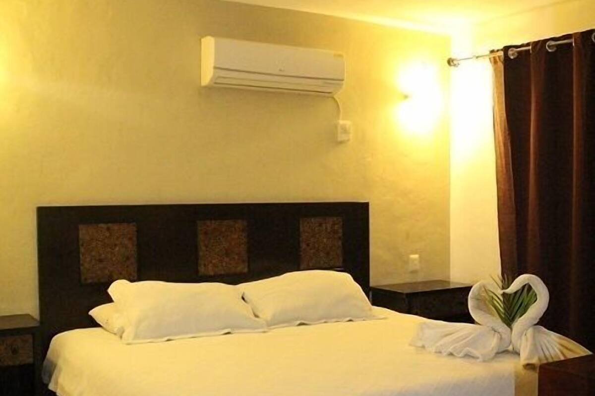 Une chambre d’hôtel équipée d’un lit, d’une table de chevet, d’un climatiseur et d’un luminaire fixé au mur.