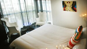 Une chambre d’hôtel avec un grand lit, une chaise blanche, une petite table et un tableau au mur.