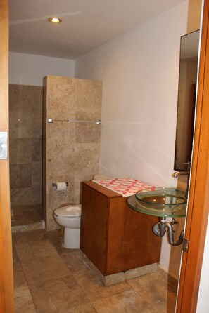 Casa de banho com lavatório de vidro, sanita e cabine de duche.