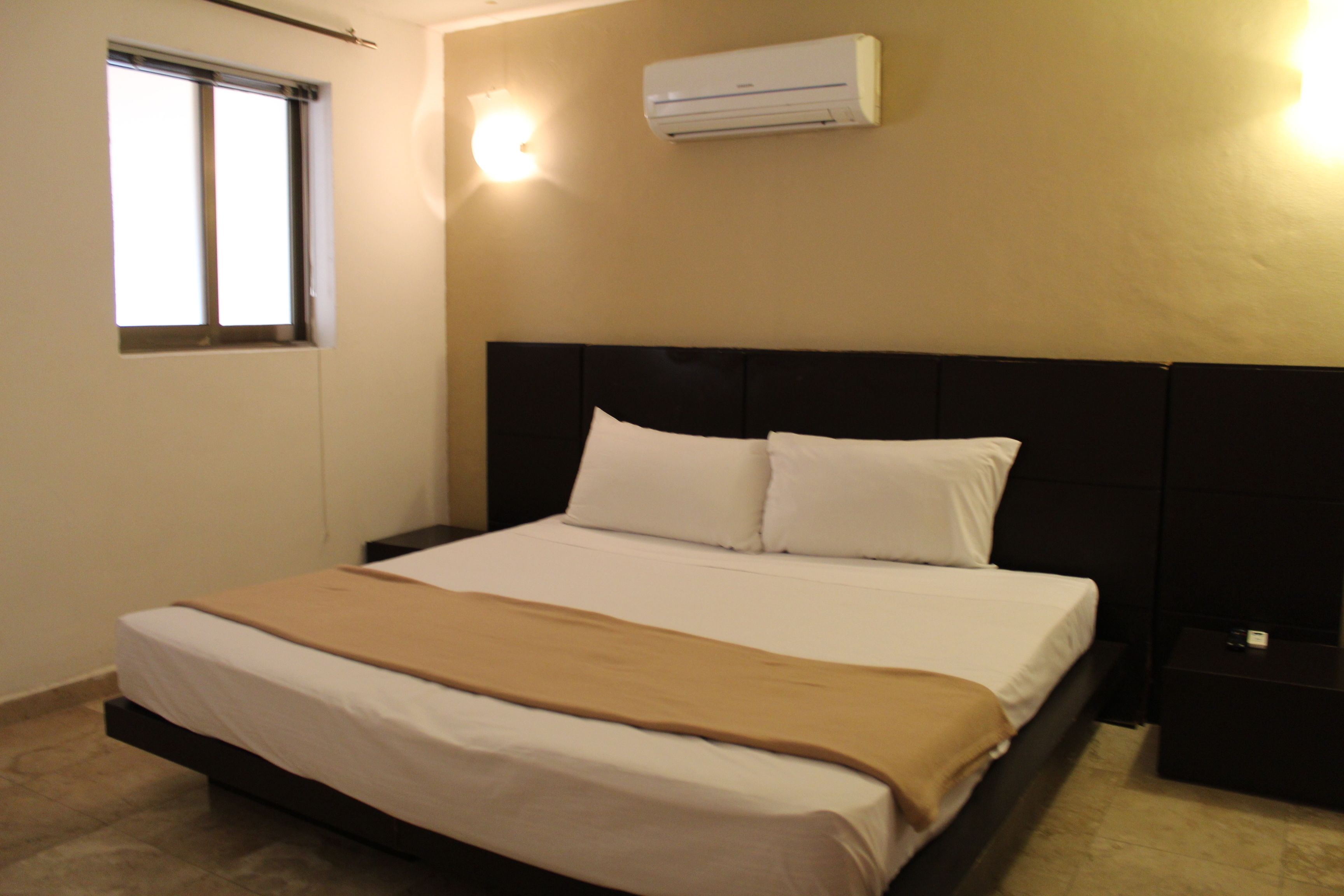 Ein Hotelzimmer mit einem Bett, einem Fenster, einer Klimaanlage und einem Nachttisch.