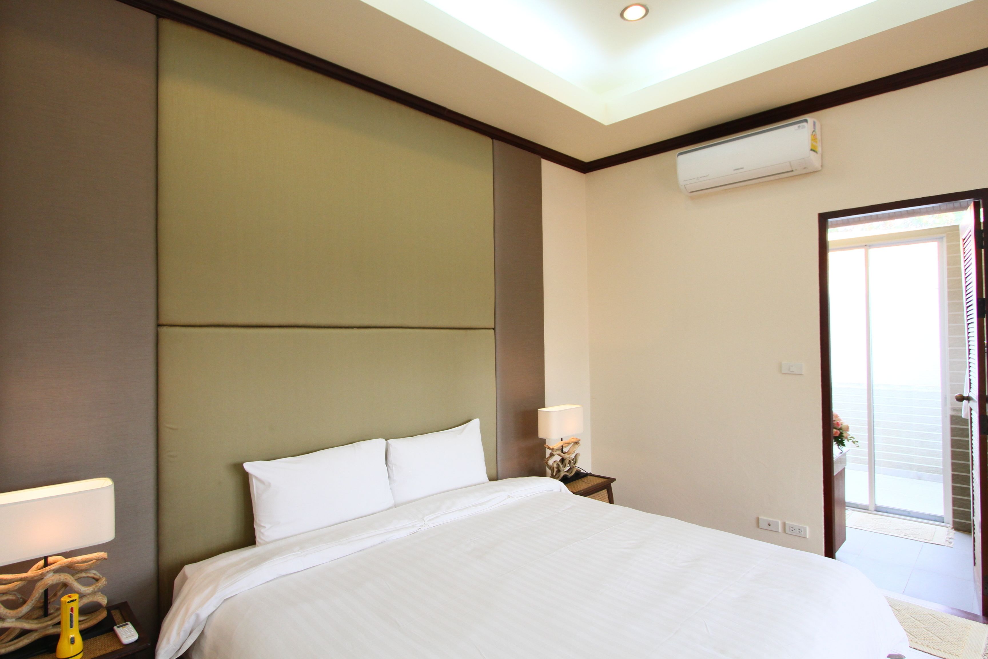 Habitación de hotel con una cama grande, una mesita de noche con lámpara, aire acondicionado instalado en la pared y una puerta que da a un balcón.