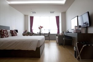 Una habitación de hotel con una cama grande, un escritorio con una silla, un televisor montado en la pared y una ventana con cortinas.
