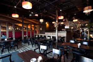 A restaurant with multiple tables and chairs, wooden panel walls, and hanging pendant lights.