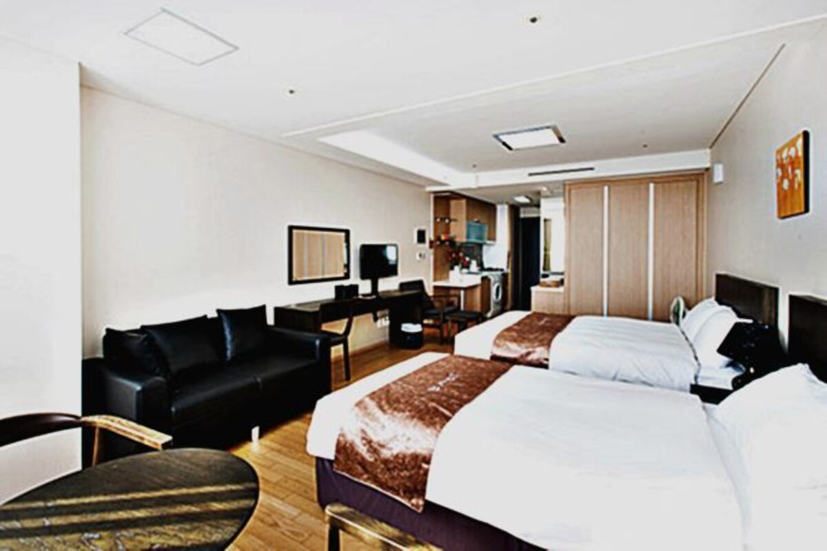 A hotel room with two beds, a sofa, a desk, and a kitchenette.