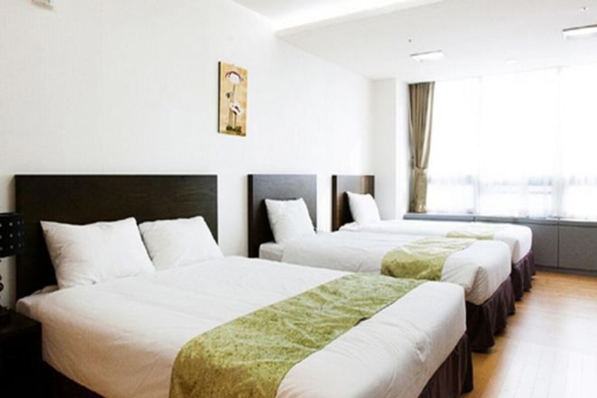 A hotel room with two beds, a window with curtains, and a painting on the wall.