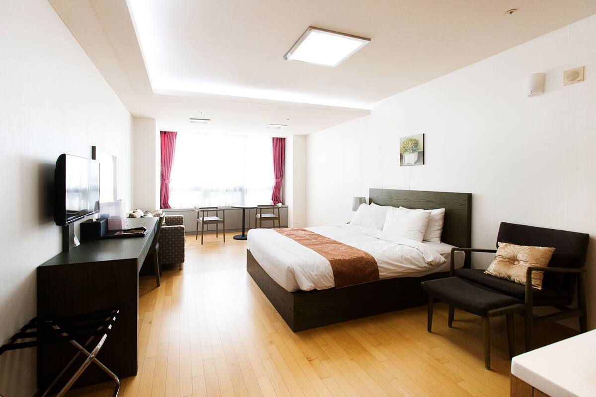 A hotel room with a bed, a desk, a chair, a TV, and a window with curtains.