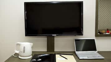 Un televisor Samsung, una computadora portátil, una tetera eléctrica blanca y una libreta sobre una mesa de madera.