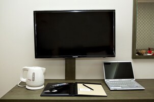Un televisor Samsung, una computadora portátil, una tetera eléctrica blanca y una libreta sobre una mesa de madera.