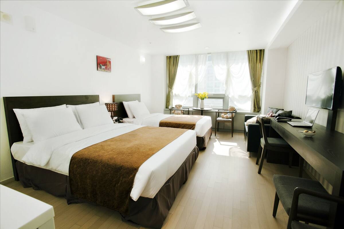 A hotel room with two beds, a desk, a chair, a TV, and a window with curtains.