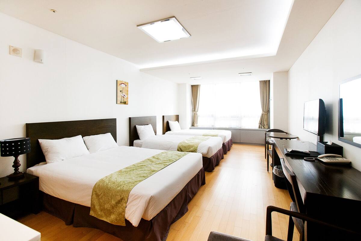 A hotel room with two beds, a desk with a TV, and a window with curtains.