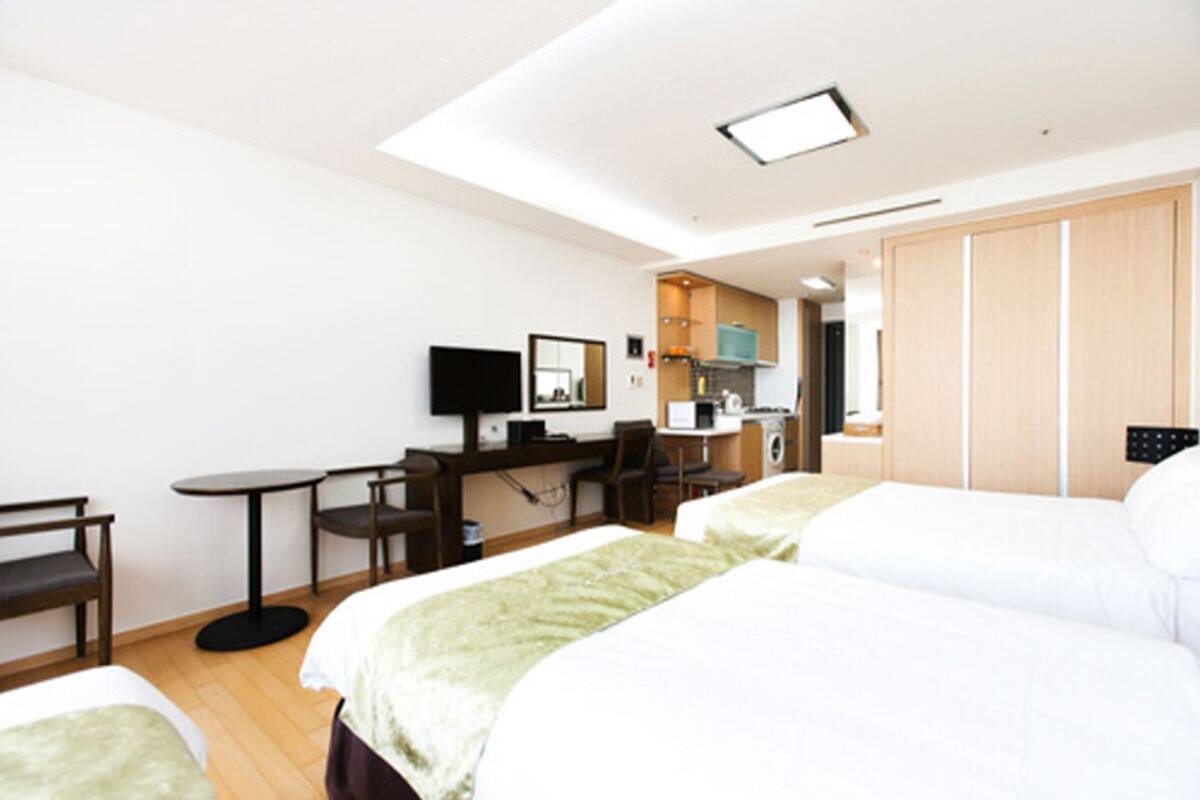 A hotel room with two beds, a desk with a computer, a chair, a TV, and a wardrobe.