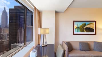 A hotel room with a large window offering a city view, a sofa, a lamp, and a framed picture on the wall.