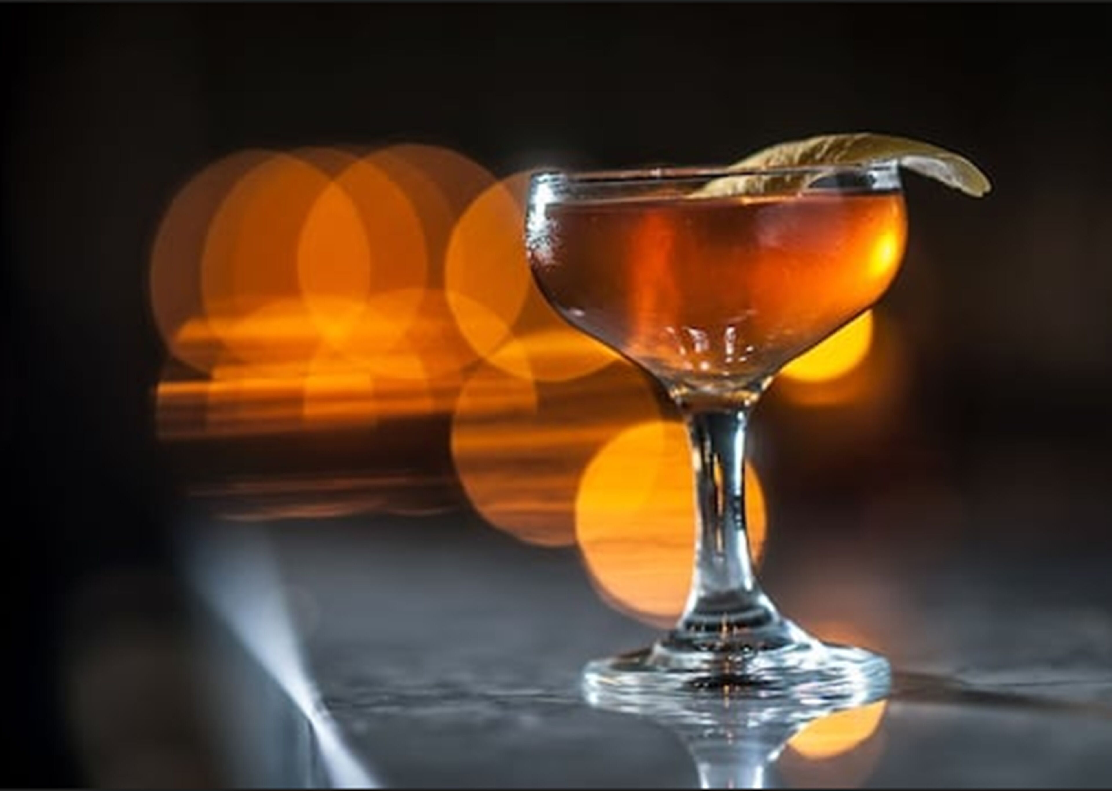 A cocktail glass with a garnish on a reflective surface.