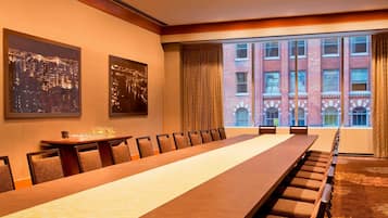 Una sala de conferencias con una larga mesa, sillas, cuadros de un paisaje urbano enmarcado y un amplio ventanal con vista a un edificio de ladrillo.