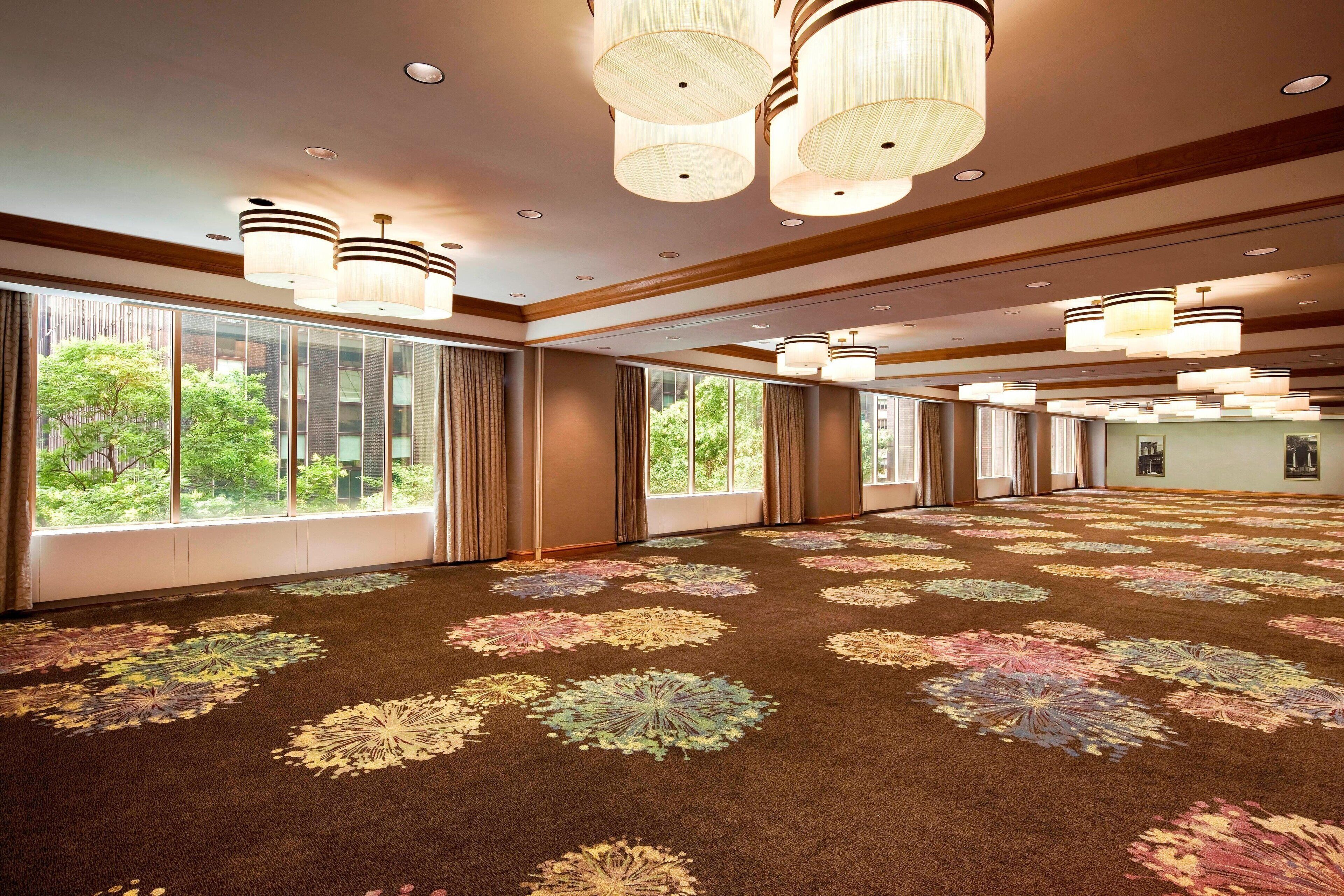 Una habitación de hotel espaciosa con ventanas amplias, una alfombra estampada y varios candelabros.