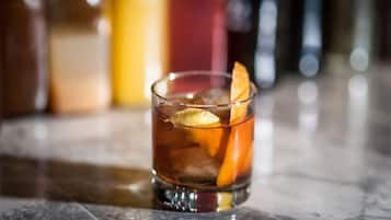 A glass with a dark beverage, ice, and an orange slice garnish on a marble surface.