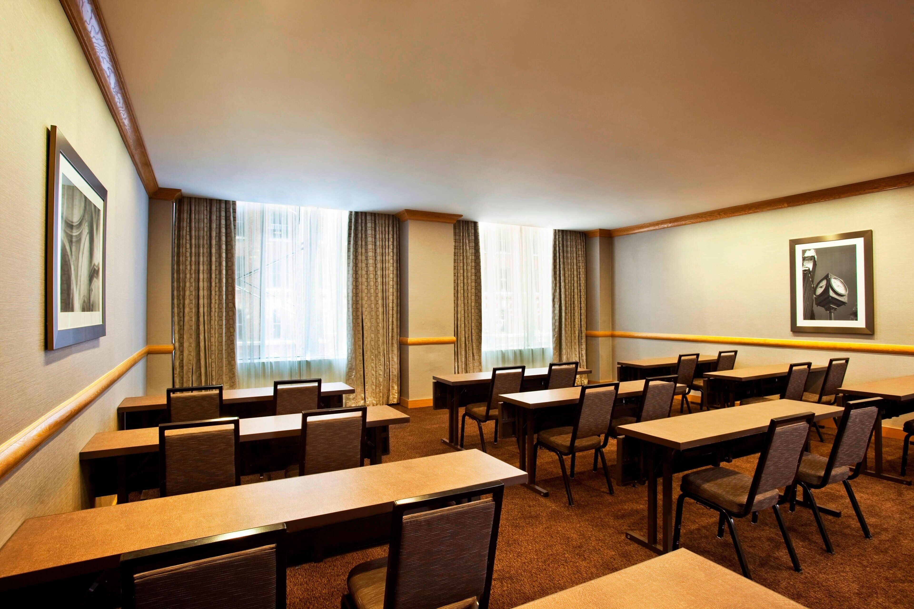 Un salón de conferencias con varias mesas y sillas, ventanas amplias con cortinas y cuadros en las paredes.