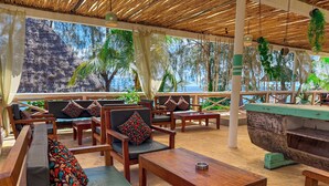 A wooden lounge area with cushioned seating, a wooden table, and a view of a natural landscape. - Paradise Beach Resort (Uroa)