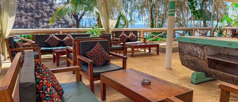 A wooden lounge area with cushioned seating, a wooden table, and a view of a natural landscape.