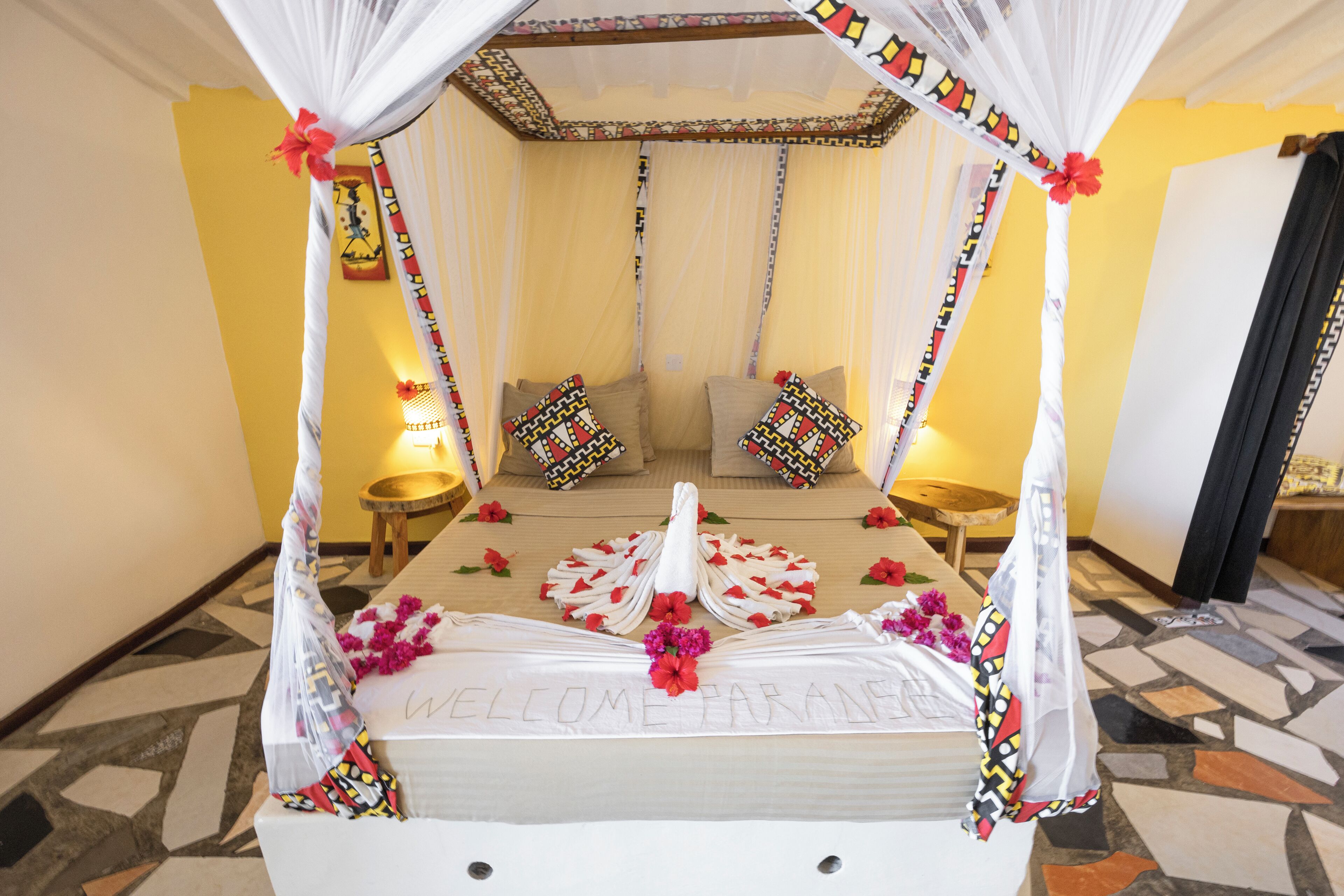A bed with a canopy, a welcome mat, and decorative pillows.