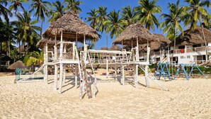 A beach with thatched-roof structures, palm trees, and a building with balconies. - Paradise Beach Resort (Uroa)