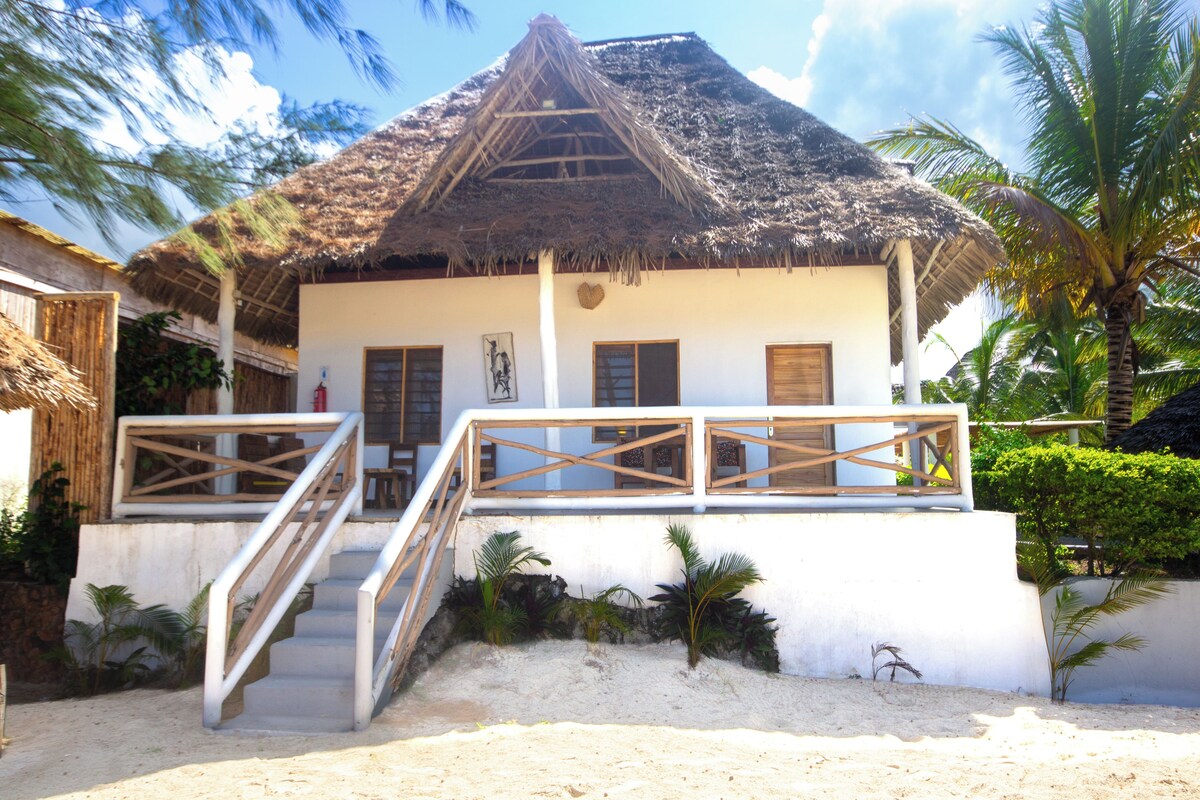 Ein strandnahes Haus mit einem Reetdach, einer Holztreppe und einer weißen Fassade.