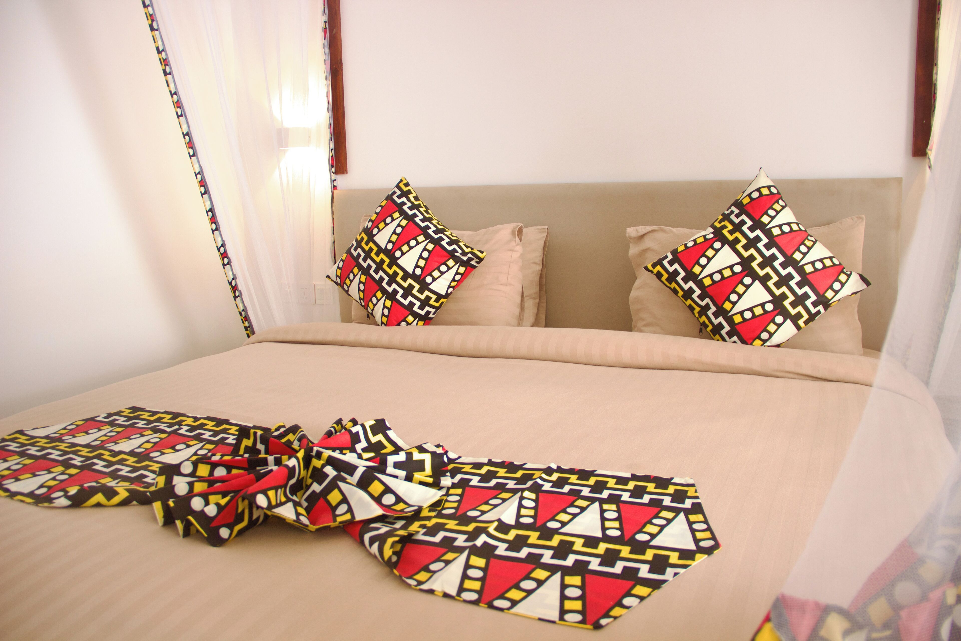 Un letto con copriletto e cuscini decorati, un comodino e una finestra con tende.