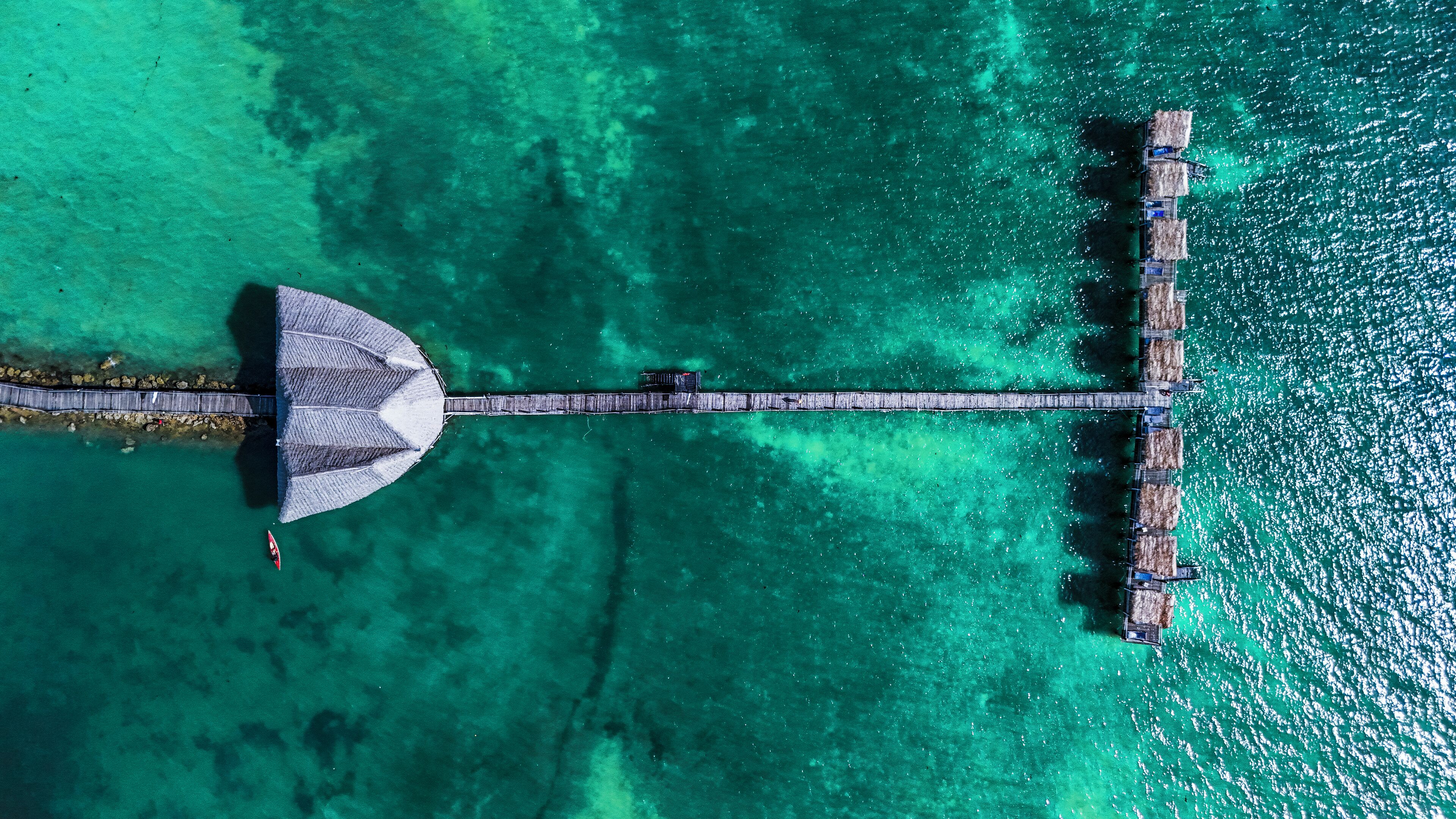An aerial view of a pier extending into turquoise waters, with a covered seating area at one end.