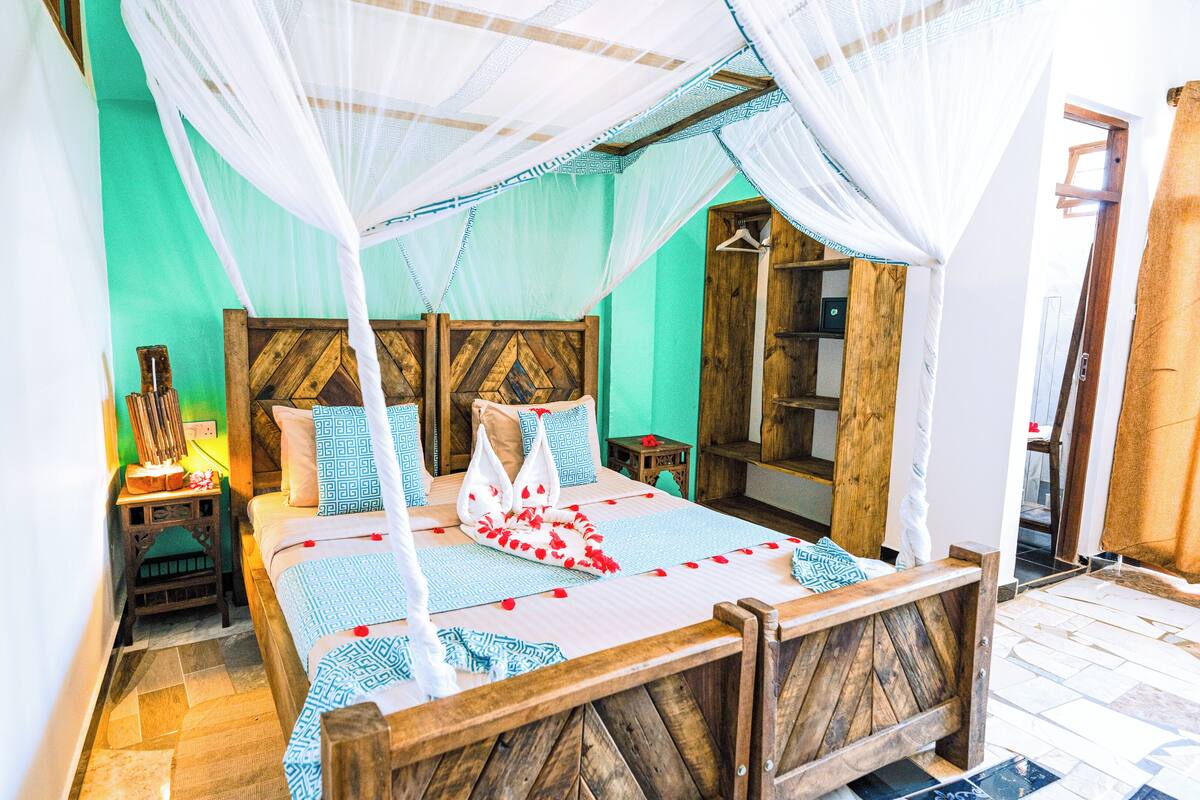 Uma cama com cabeceira de madeira, uma mesinha de cabeceira com abajur e um cabideiro.