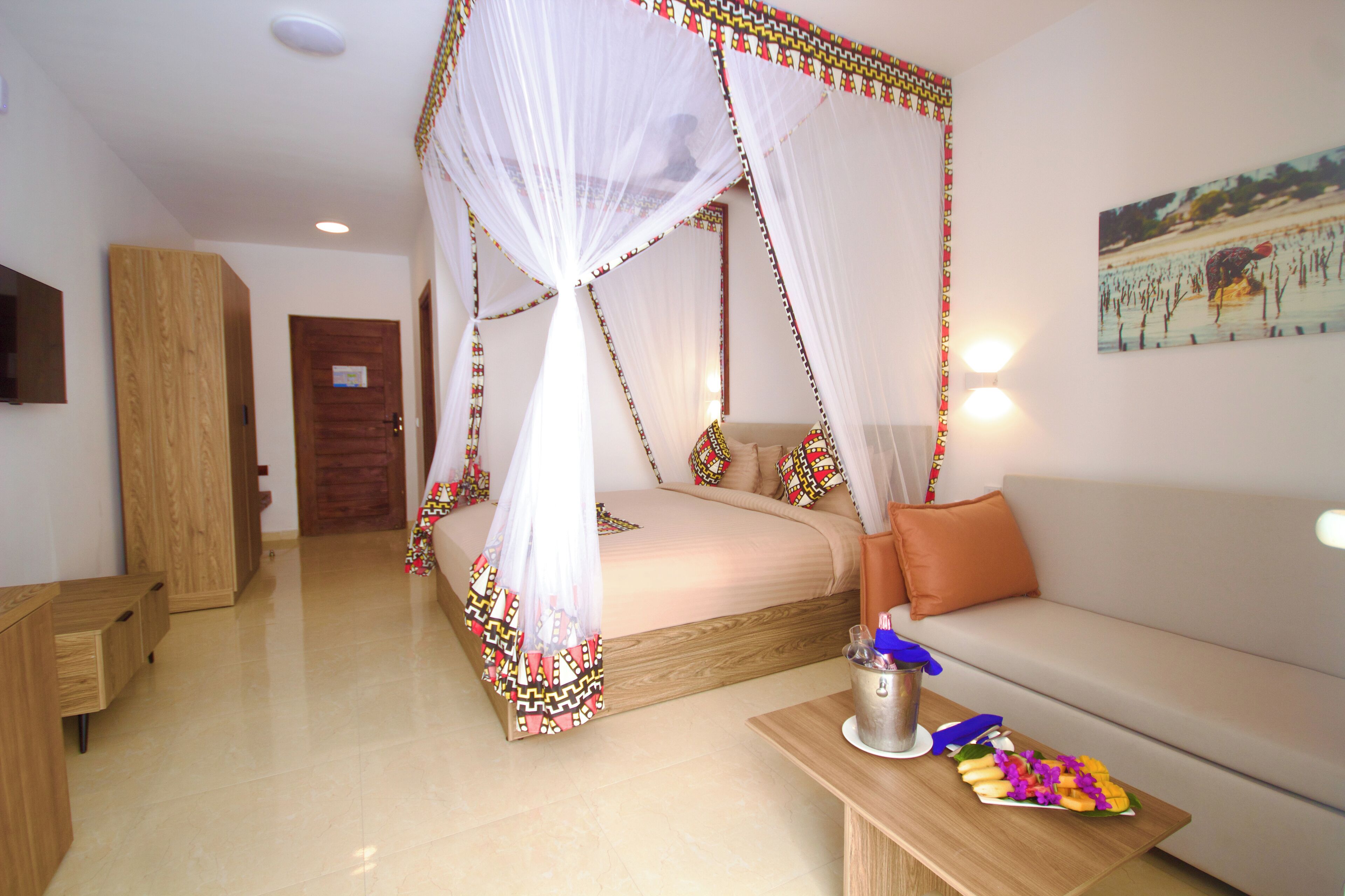 A bedroom with a four-poster bed, a sofa, a bedside table with snacks, and a wooden wardrobe.