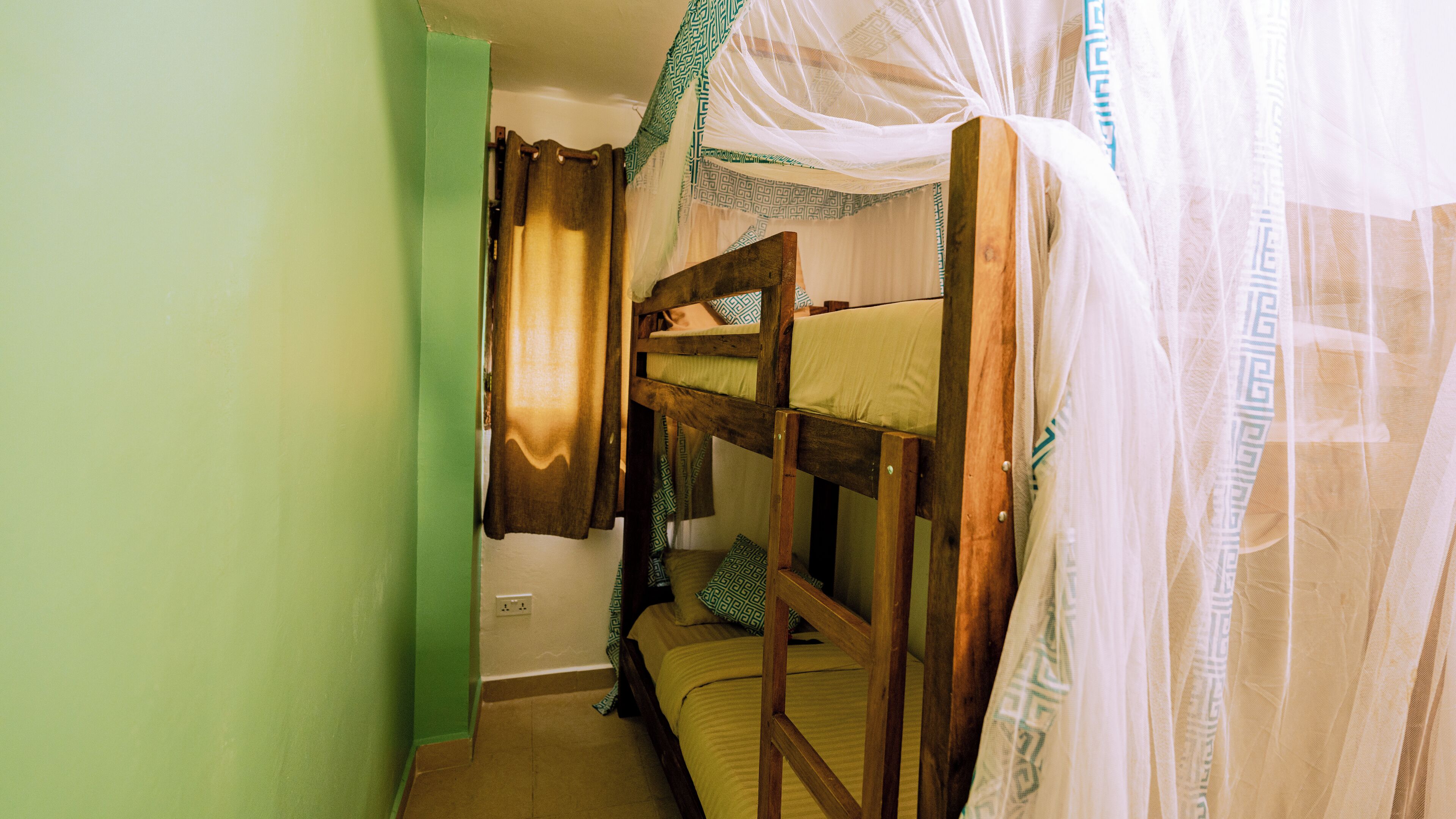 Una cama litera con mosquitero, una pared verde y un enchufe.