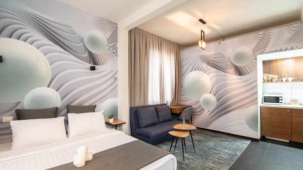 A modern hotel room with a large bed, a sofa, a small table, and a kitchenette. - 27 Montefiore TLV (Tel Aviv)