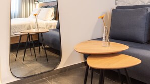 A modern hotel room with a large mirror, a small round table with a vase, a sofa, and a bed with curtains. - 27 Montefiore TLV (Tel Aviv)