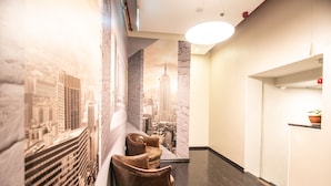 A hallway with a cityscape mural, a seating area with leather chairs, and a modern light fixture. - 27 Montefiore TLV (Tel Aviv)