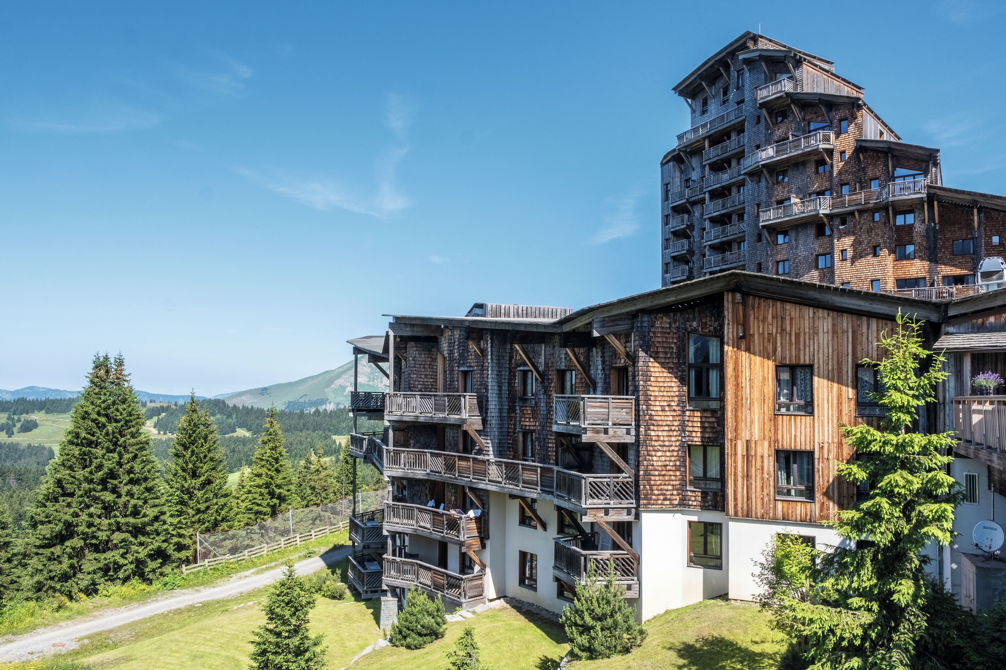 Un edificio de varios pisos con balcones, un telesilla y montañas al fondo.