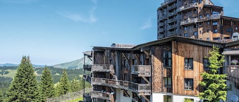 Un edificio de varios pisos con balcones, un telesilla y montañas al fondo.