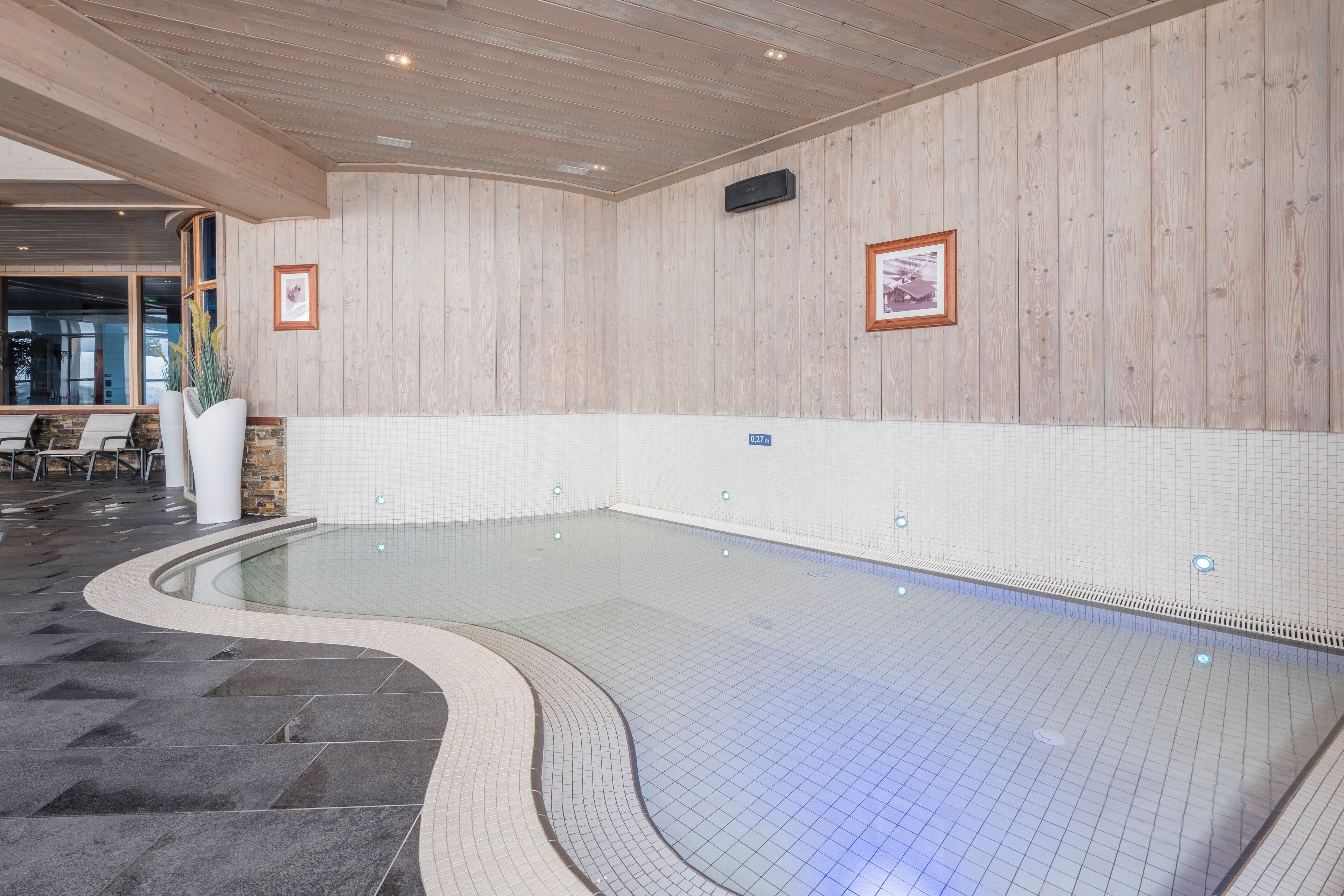A swimming pool with a tiled floor and wooden walls, surrounded by a curved stone border.