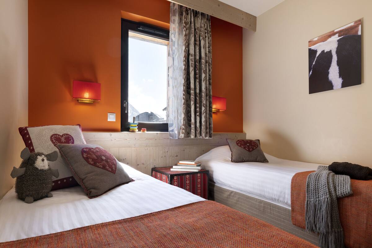 A hotel room with two beds, a window with curtains, a wall-mounted lamp, and a painting.