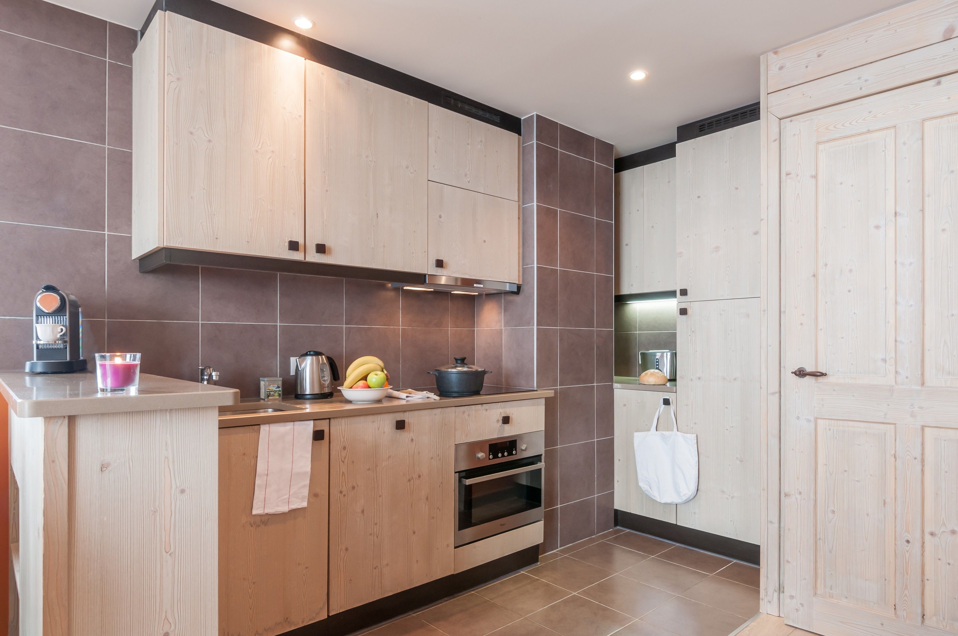 A modern kitchen with wooden cabinets, a built-in oven, and a countertop with a coffee maker and bananas.