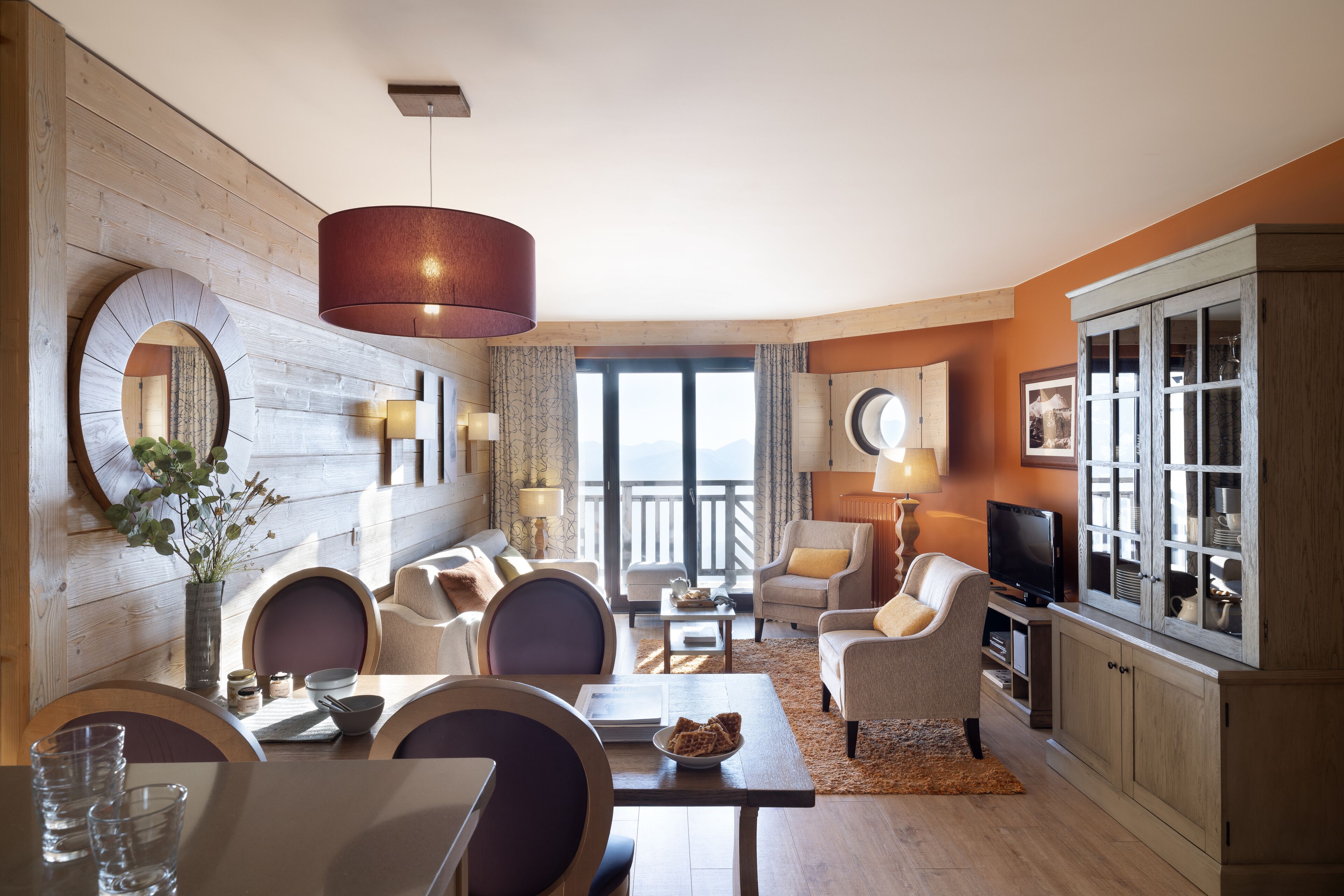 A modern living room with a wooden wall, a dining area with a table and chairs, and a television on a cabinet.