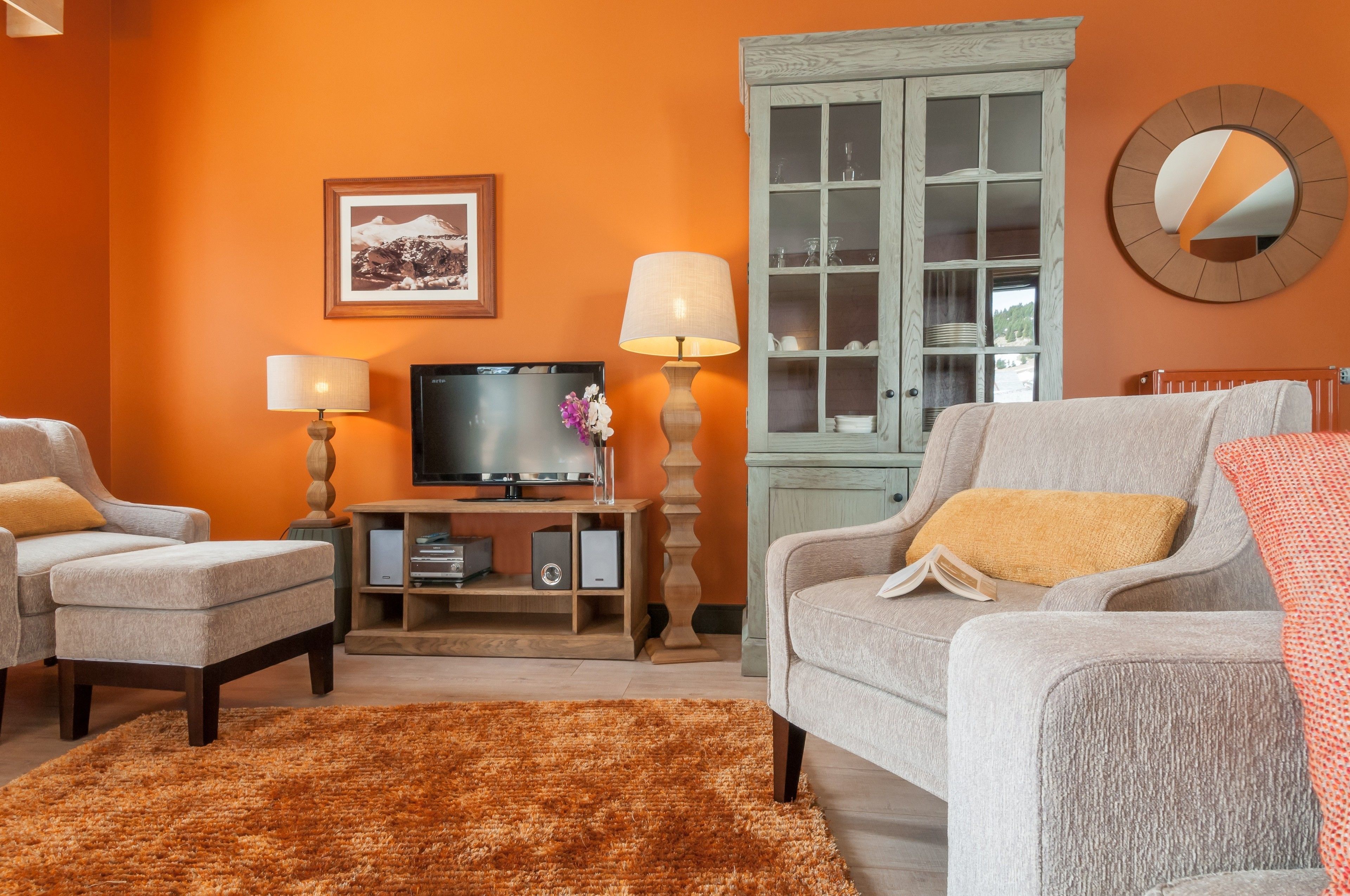 Een woonkamer met oranje wanden, een televisie, twee lampen, een kast en een bank met een kussen.