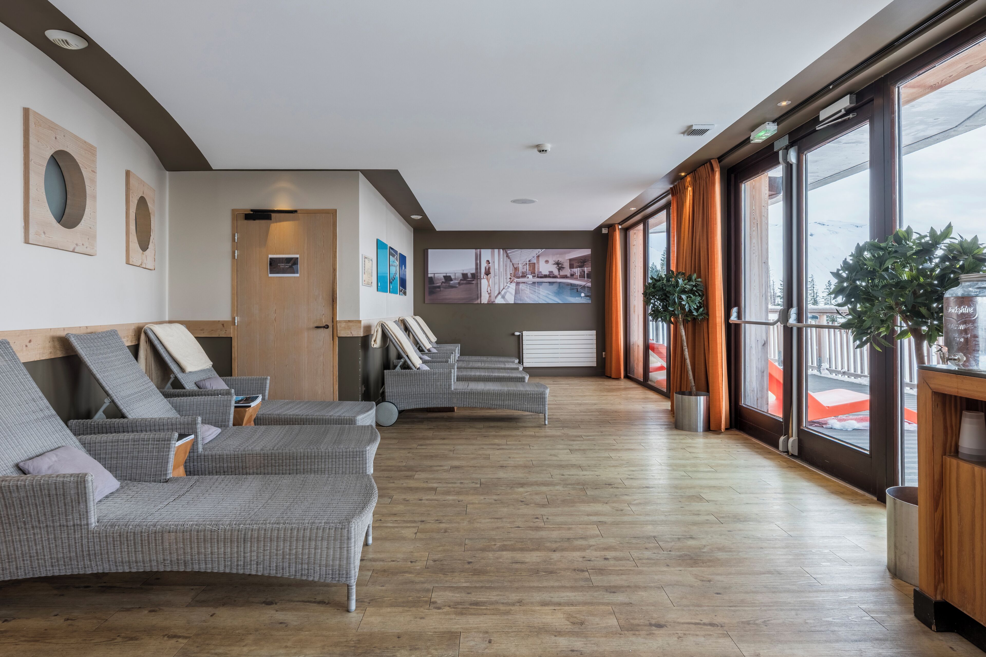 Un vestíbulo de hotel con sillones de mimbre, un ventanal con vistas a montañas y un televisor montado en la pared.