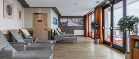 Un vestíbulo de hotel con sillones de mimbre, un ventanal con vistas a montañas y un televisor montado en la pared.