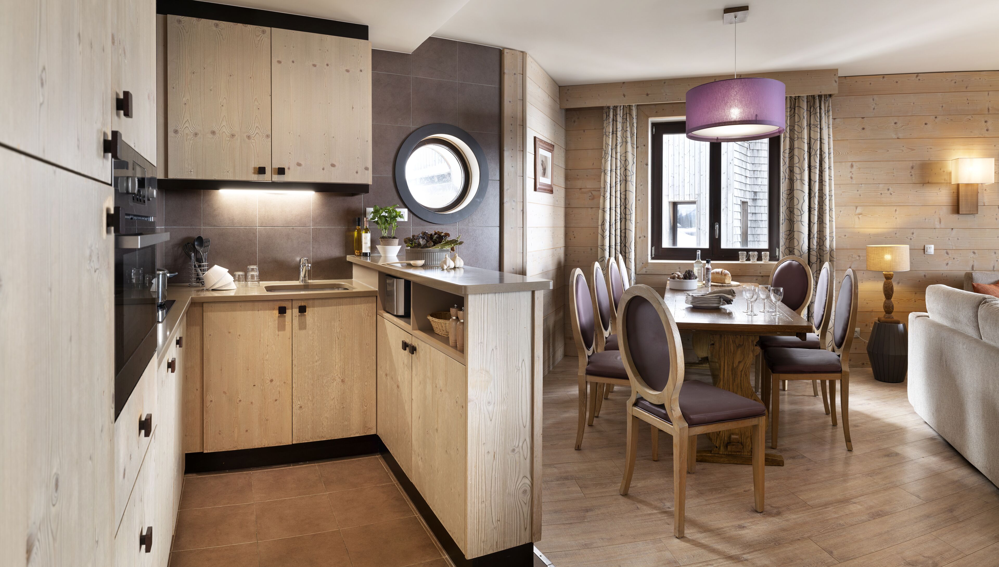 Une cuisine moderne avec des meubles en bois, un îlot central et un coin repas comprenant une table ronde et des chaises.