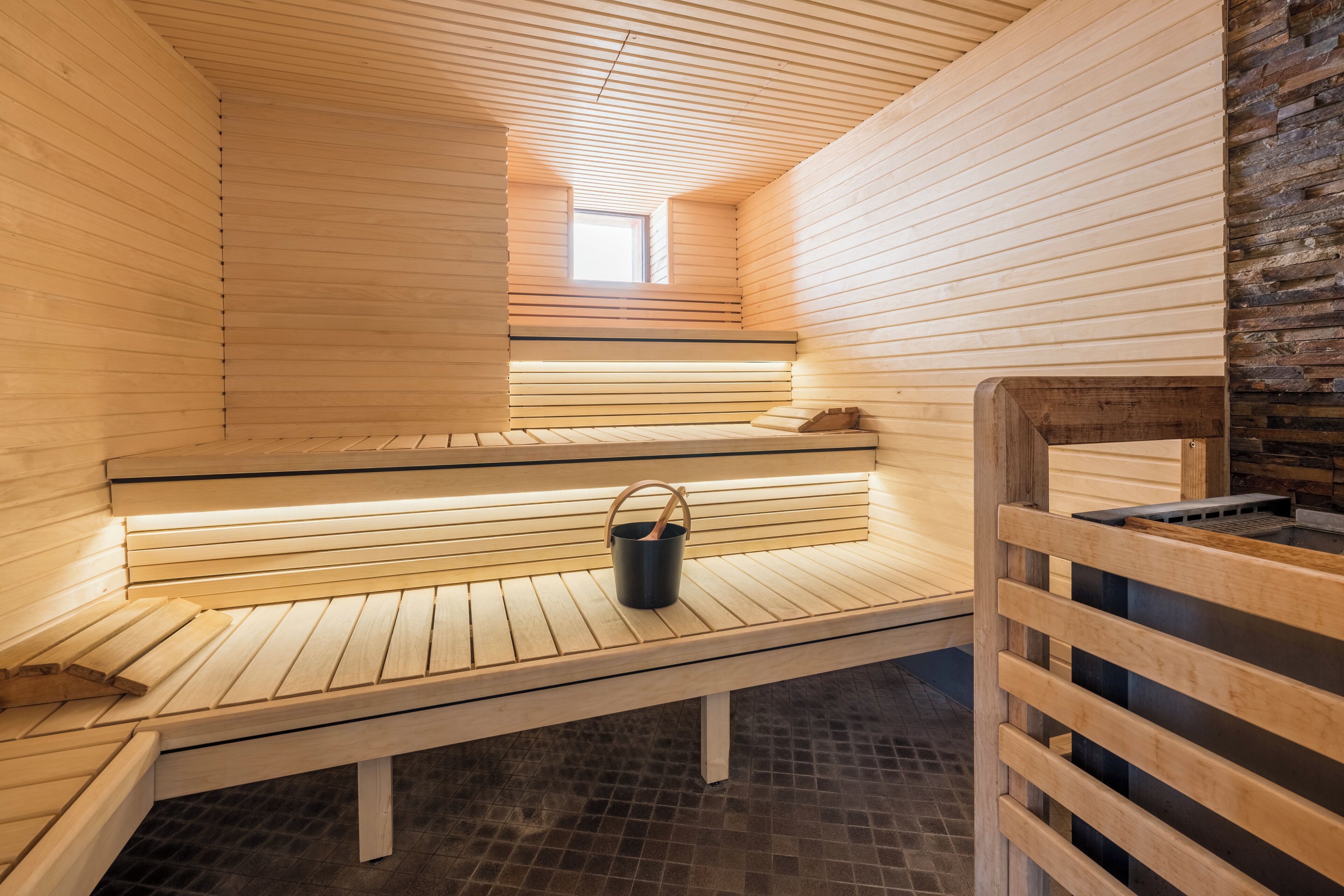 A sauna with wooden benches, a small window, and a stone wall.