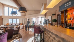 A spacious living area with a wooden floor, a bar area with a variety of bottles, and a large window providing natural light. - Résidence Pierre & Vacances Premium L'Amara (Avoriaz)