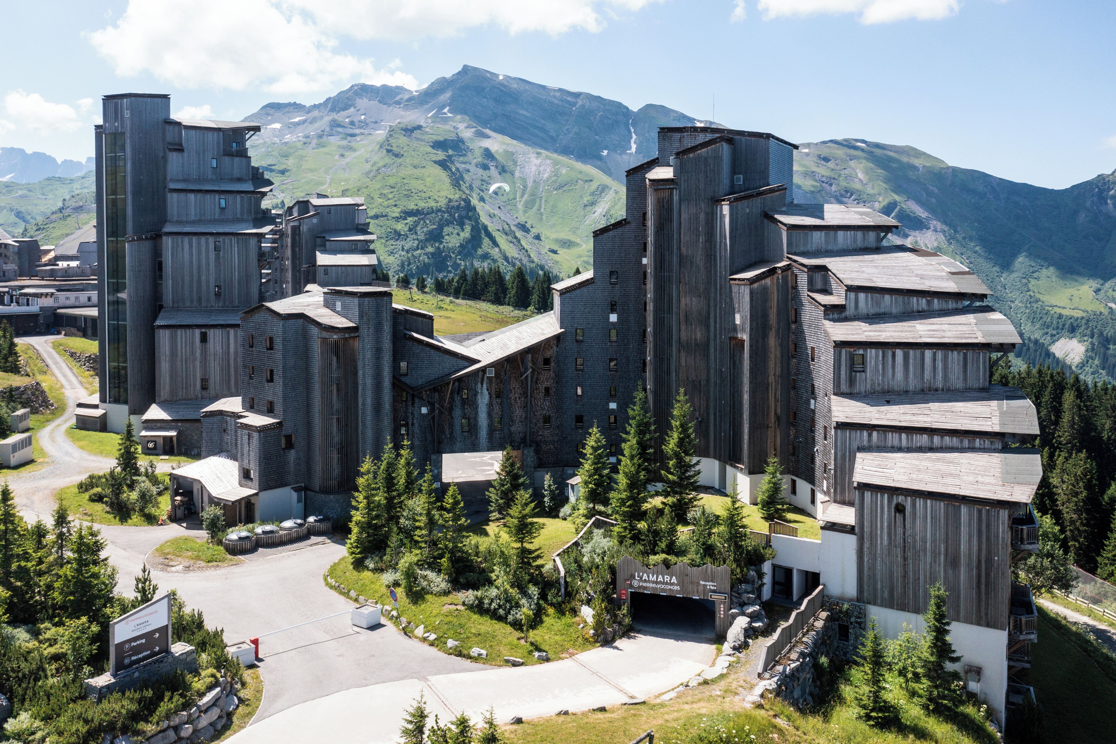 Un edificio moderno con un diseño arquitectónico único, rodeado de exuberante vegetación y montañas al fondo.
