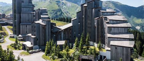 Un edificio moderno con un diseño arquitectónico único, rodeado de exuberante vegetación y montañas al fondo.